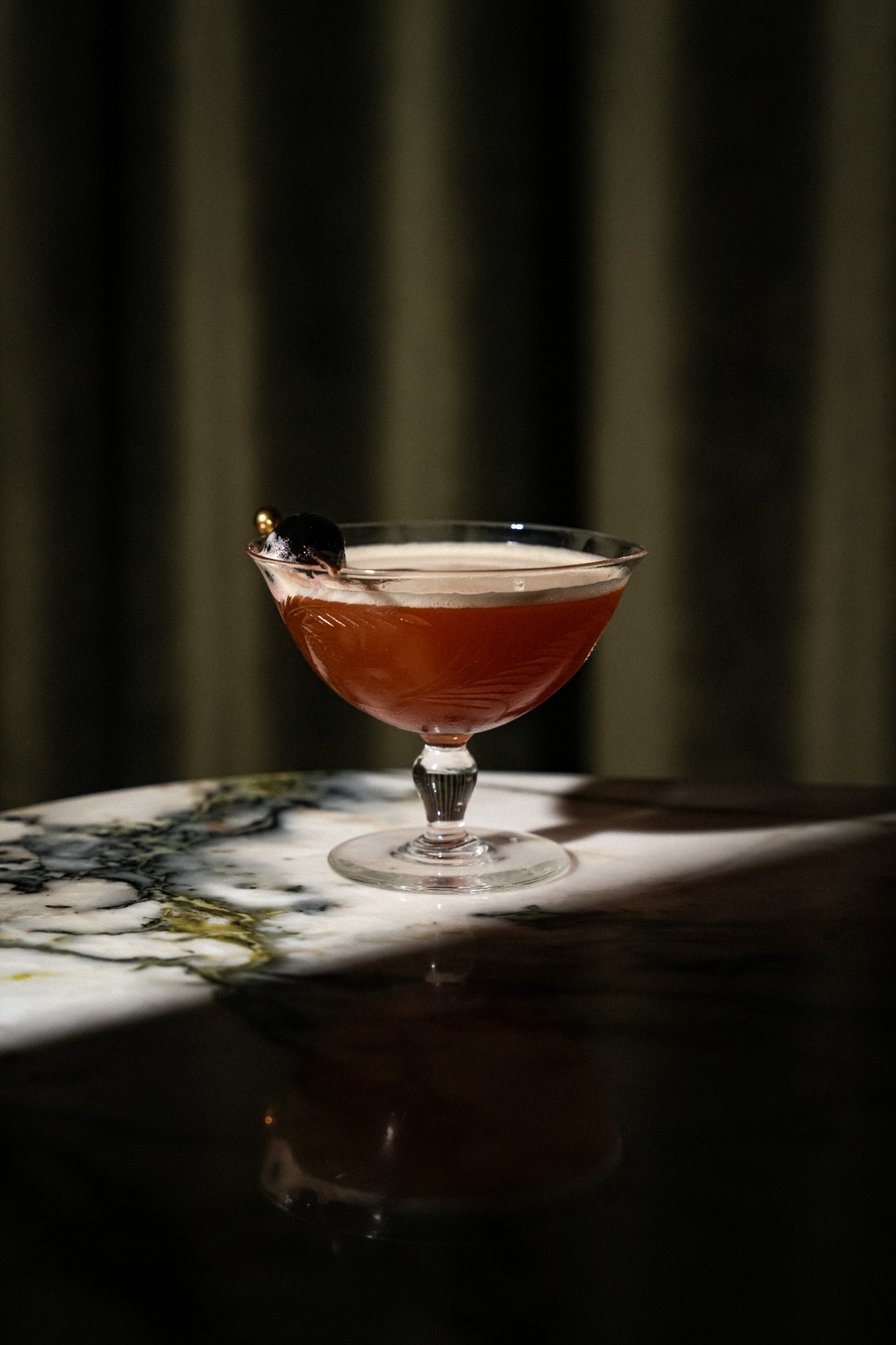 An amber-red cocktail in a patterned coupe on the marble bar at Parquet